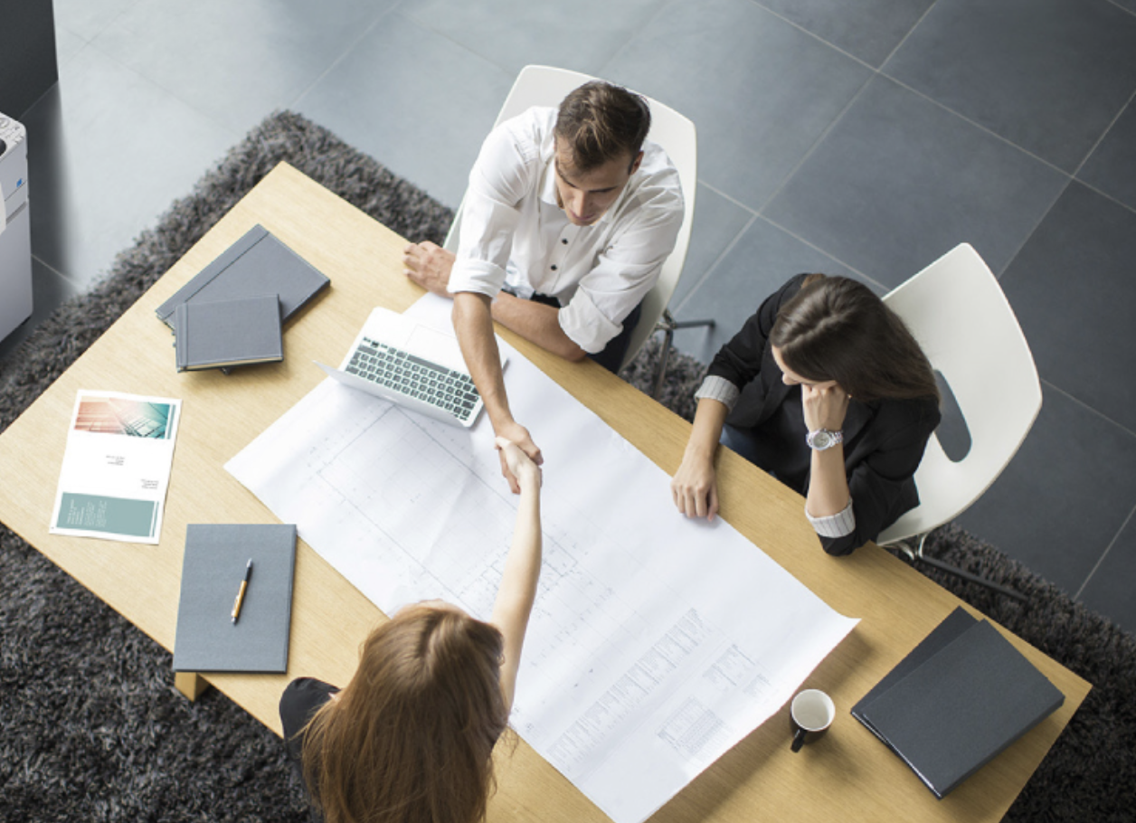 Business people at desk shaking hands in modern workspace setting